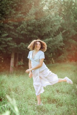 Uzun beyaz elbiseli güzel mutlu bir kız çayıra atlıyor ve gülüyor. Seçici odaklanma. Vintage fotoğraf.