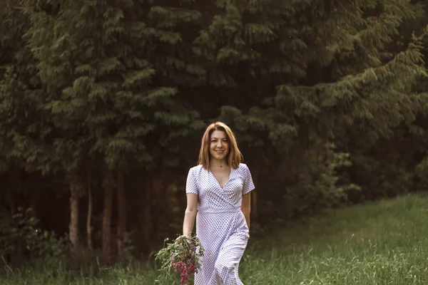 一个穿着白衣的美丽而快乐的女孩手里拿着一束野花 一个身材苗条的女孩的画像 她的身上带着一束野花 选择性焦点 — 图库照片