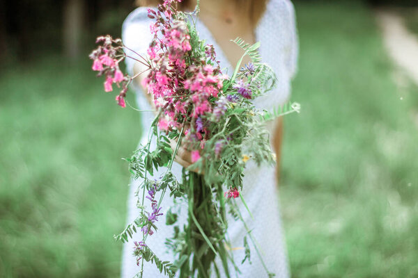A married woman holds out a bouquet of wild flowers to the camera. The hand of a woman with an engagement ring holds lilac wildflowers. Selective Focus.