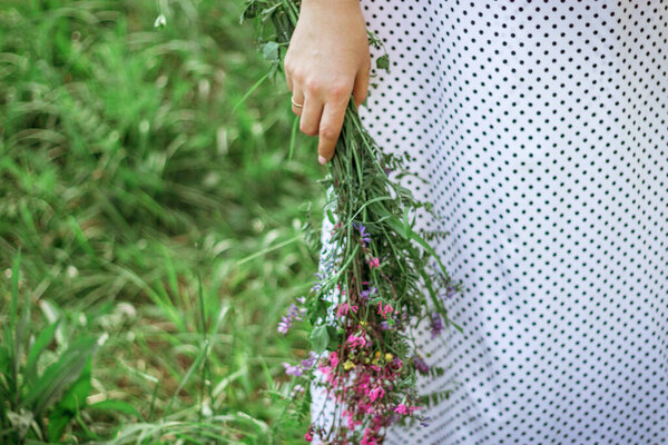 A beautiful woman in a white dress collects wildflowers in a summer meadow, close-up. An atmospheric moment. A stylish young woman in a rustic dress is picking flowers in the countryside. Slow life.