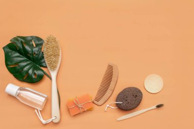 Sıfır atık taraklı banyo aksesuarları, ahşap diş fırçası, katı sabun, kozmetik kavanozu, ahşap tarak, bej arka planda bir yaprak dolusu canavar olan sünger..