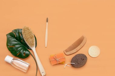 Sıfır atık taraklı banyo aksesuarları, ahşap diş fırçası, katı sabun, kozmetik kavanozu, ahşap tarak, bej arka planda bir yaprak dolusu canavar olan sünger..