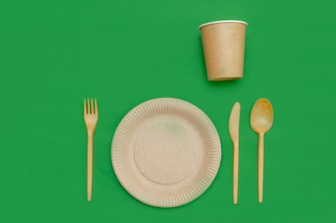 Yeşil arka planda geri dönüşümlü çatal, kaşık, bıçak, tabak ve bardak. Mutfak aletleri. Üst Manzara. Minimalist stil. Boşluğu kopyala.