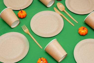 Geri dönüşümlü çatal, kaşık, bıçak, tabak ve bardak yanında turuncu balkabağı olan yeşil bir arka planda. Mutfak gereçleri masada servis edilir. Üst Manzara. Minimalist stil. Boşluğu kopyala.