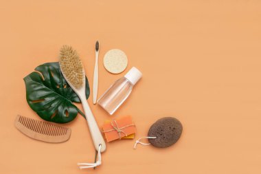 Sıfır atık taraklı banyo aksesuarları, ahşap diş fırçası, katı sabun, kozmetik kavanozu, ahşap tarak, bej arka planda bir yaprak dolusu canavar olan sünger..