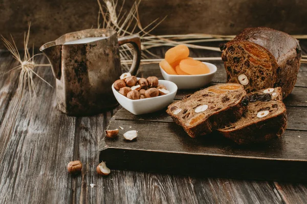 Sütlü rustik kahvaltı, kurumuş meyveli ekmek, fındık ve koyu arkaplanda kurutulmuş kayısılar.