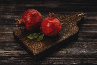 Koyu arkaplanda tahta bir tahtada iki kırmızı nar. 