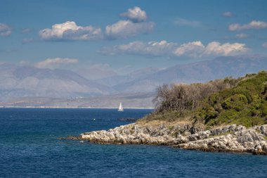 Yaz sonunda sakin bir İyon denizi. Arkadaki Arnavut dağları. Beyaz bulutlu mavi gökyüzü. Korfu (Korfu), Siky Körfezi, Yunanistan