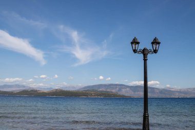 İyon Denizi kıyısındaki gezinti güvertesinde çift fener manzarası. Ufuktaki Arnavut dağları. açık beyaz bulutlu mavi gökyüzü. Kouloura, Kalami, Korfu (Korfu), Yunanistan.