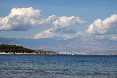Küçük dalgalı İyon Denizi suyu. Ufuktaki Arnavut dağları. Açık beyaz bulutlu mavi gökyüzü. Kouloura, Kalami, Korfu (Korfu), Yunanistan.