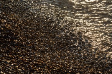 Gelgitte çapraz görüş. Parlak, ıslak çakıl taşları ve gün batımında İyon denizinin dalgaları. Acharavi, Korfu Adası (Korfu), Yunanistan