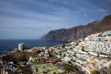 Şehrin bir parçası. Arka planda Los Gigantes uçurumları var. Sonbaharda bulutlu mavi gökyüzü. Puerto de Santiago, Tenerife, Kanarya Adaları, İspanya.