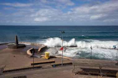 Deniz feneri olan şehir plajı. Sonbaharda Atlantik okyanusunun büyük dalgaları. Beyaz bulutlu mavi gökyüzü. Bajamar, Santa Cruz, Tenerife, İspanya.