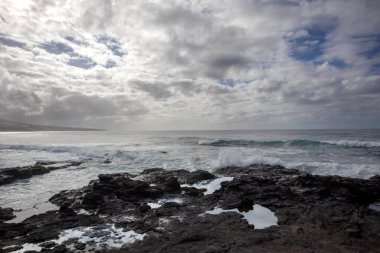 Volkanik siyah lav kayalarından oluşan doğal sahil. Sonbaharda dalgalı Atlantik Okyanusu. Yoğun bulutlu mavi gökyüzü. Punta de Hidalgo, Santa Cruz, Tenerife, Kanarya Adaları, İspanya.