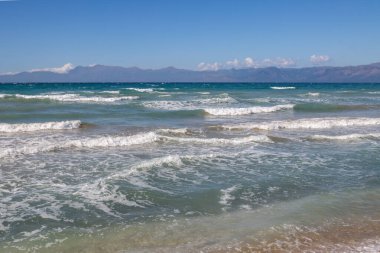 Yaz sonunda dramatik dalgalarla dolu İyon Denizi. Arkadaki Arnavut dağları. Beyaz bulutlu mavi gökyüzü. Korfu Adasının Kuzeyi (Korfu), Acharavi, Yunanistan.