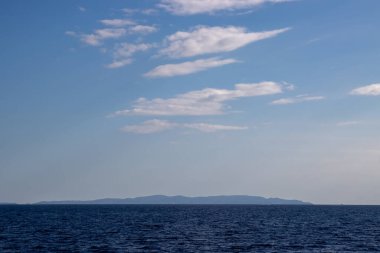 Derin mavi İyonya 'daki bir tekneden Paxos adası manzarası. Beyaz bulutlu mavi gökyüzü. Paxos, Yunanistan.