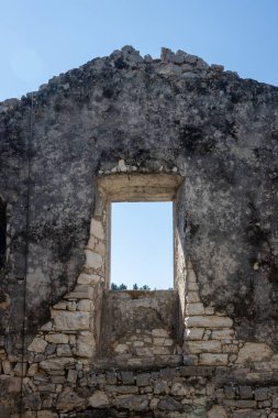 Eski pencereli terk edilmiş bir evin taş duvarı. Çatı çizgisi. Parlak mavi gökyüzü. Paxos, Yunanistan.