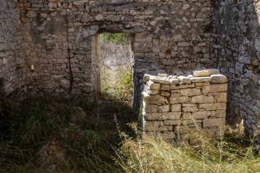 Taştan yapılmış terk edilmiş bir evin içinde. Zemin çimen ve kapı yerine delik açmak yerine. Mükemmel istiflenmiş ve hizalanmış taş yığını. Paxos, Yunanistan.