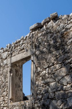 Eski pencereli terk edilmiş bir evin taş duvarı. Çatı çizgisi. Parlak mavi gökyüzü. Paxos, Yunanistan.