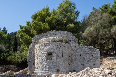 Ayia Marina 'nın erken dönem Christina Bazilikası' nın yıkıntıları. Etrafı taze ağaçlarla çevrili. Güneşli bir gün, mavi gökyüzü. Paxos, Yunanistan