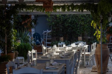 Tencerelerde çeşitli bitkilerle çevrili bir restoranın terası. Bulaşık takımlarıyla aydınlanmış beyaz masalar, misafirler için hazır. Gaios, Paxos, Yunanistan.