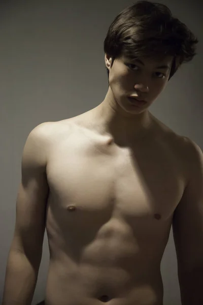 Tişörtsüz genç adam düşünceli görünüyor.