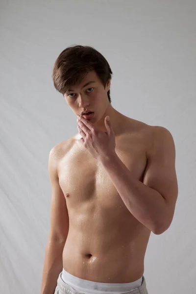 Tişörtsüz genç adam düşünceli görünüyor.