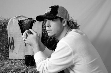 Düşünceli kovboy elinde bir saman balyasıyla oturuyor