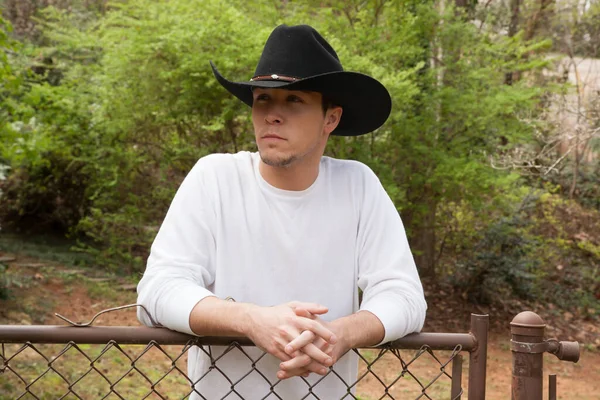 Çitlerdeki batılı şapkalı yakışıklı adam.