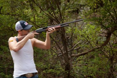 Yakışıklı adam pompalı tüfek doğrultuyor.