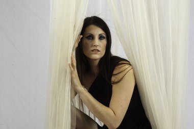 Güzel bir kadın perdeyle düşünceli bir şekilde oynuyor.