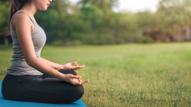 Asyalı kadın meditasyon yapıyor ve lotusta oturuyor. Parkta poz veriyor, Sağlıklı ve Yoga Kavramı, Zihin-Vücut Geliştirme Konsepti, Seçici Odaklanma, Boşluğu Kopyalama.