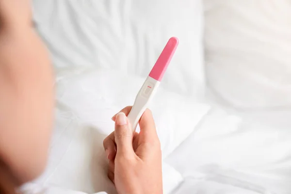 Unhappy young asian woman holding pregnancy test showing a negative result in her bedroom, wellness and healthy concept, infertility problem,Selective focus.