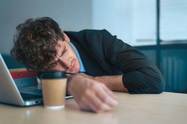 Yorgun işadamı bütün gün çalıştıktan sonra kahve fincanıyla ofis masasında kestiriyor..