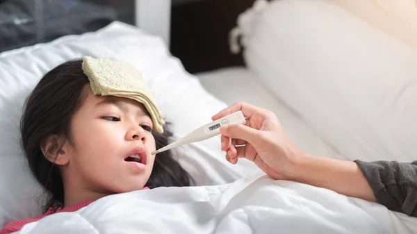 アジアの母親は 午前中にベッドの上で彼女の口の中にデジタル温度計を持つ温度の女の子を測定し 病気の子供は 熱を減らすためのクールなタオルを持っています 選択的な焦点 健康と感染の概念 — ストック写真