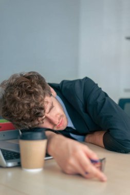 Yorgun işadamı bütün gün çalıştıktan sonra kahve fincanıyla ofis masasında kestiriyor..
