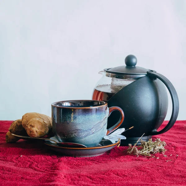 Çaydanlık, kupa ve zencefil üzerinde kırmızı bir masa örtüsü