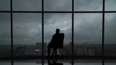 İş adamı yağmurlu arka planda sandalyede dönüyor.