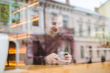 Kafenin camında telefonu olan mutlu adam.