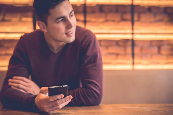 The happy man sitting with a phone at the restaurant table