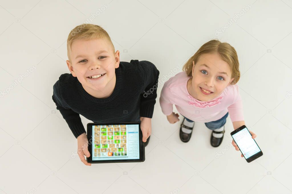 The two happy kids stand with devices. View from above