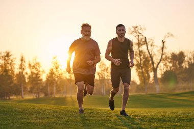 Gün batımında çimlerde koşan iki sporcu.