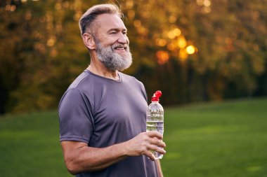 Yaşlı adam elinde bir şişe su tutuyor.