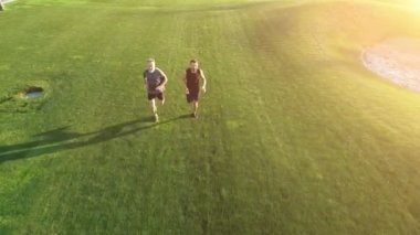 Güneşli arka planda, güzel bir parkta çimlerin üzerinde koşan iki adam.