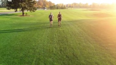 Baba ve oğlu resimli bir parkta çimlerde koşuyorlar.