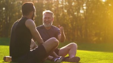 Mutlu baba ve oğlu parkta çimlerin üzerinde oturup konuşuyorlar. yavaş çekim