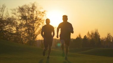 Parkta gün batımında koşan iki adam. yavaş çekim