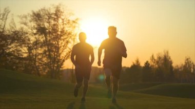 Parkta koşan iki adam güzel bir günbatımı arka planında. yavaş çekim