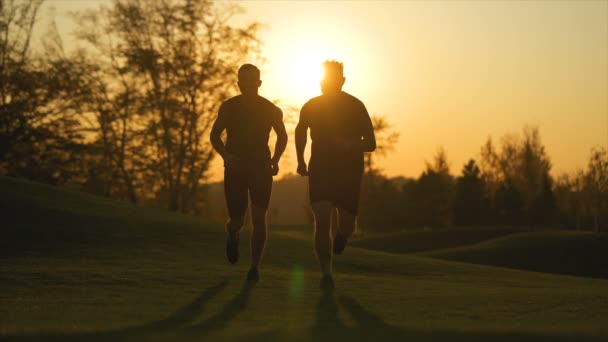 美しい日の出を背景に公園を走っている二人の男 スローモーション — ストック動画