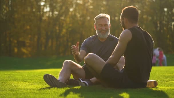 幸せな父と息子は草の上に座って話しています スローモーション — ストック動画